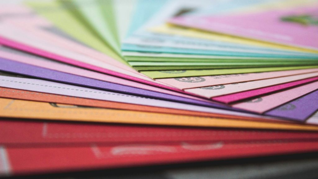 Pile de feuilles de papier colorées, superposées en éventail, avec différentes teintes de rose, violet, vert et orange.